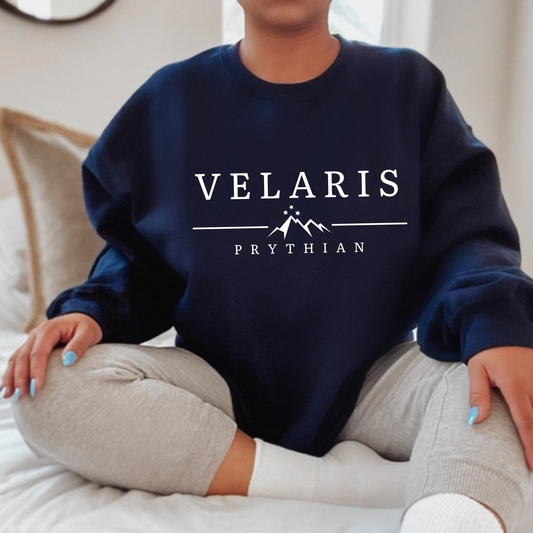 Model seated on a bed in a navy Velaris Prythian sweatshirt, ACOTAR merch inspired by Sarah J. Maas