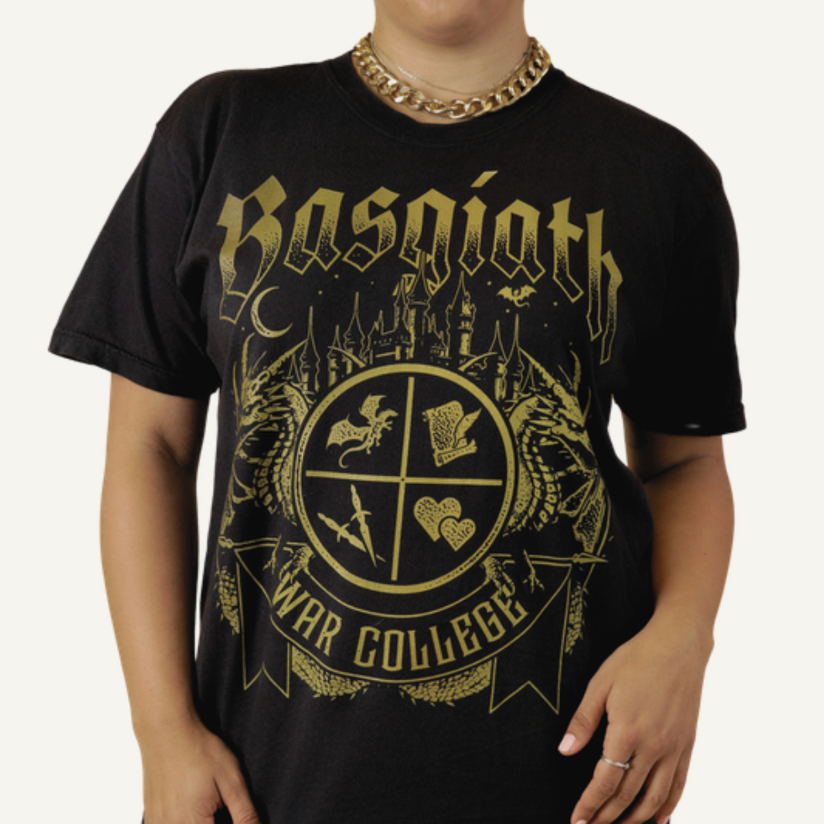 Model wearing the black Basgiath War College t-shirt, gold gothic Basgiath lettering over the War College crest with dragons, Fourth Wing merch inspired by Rebecca Yarros