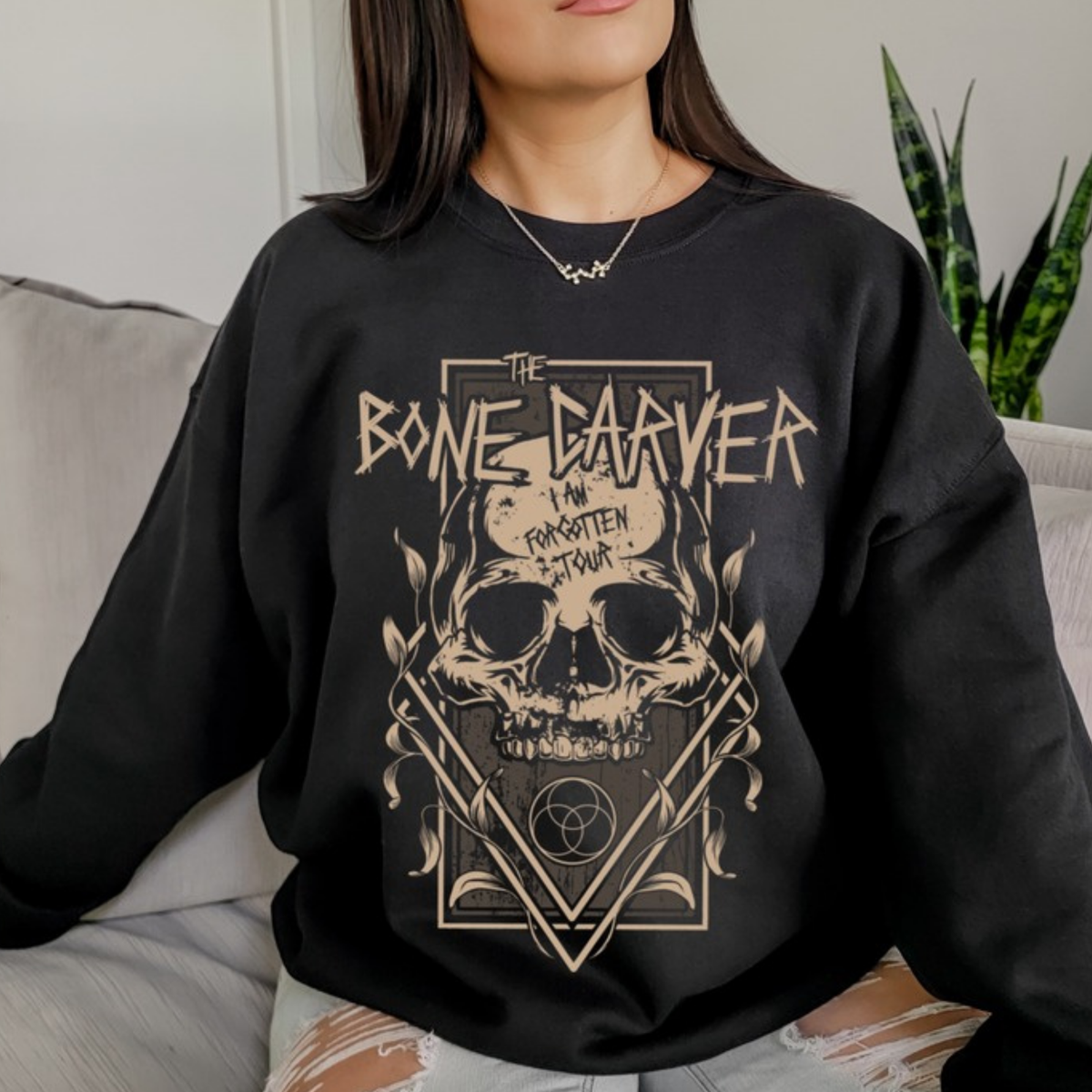 Bone Carver Sweatshirt in black on a model seated on a grey sofa. ACOTAR merch.