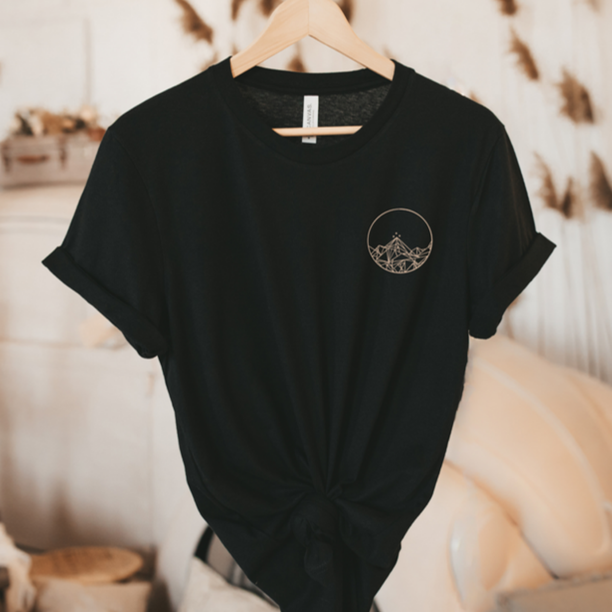 Black Feyres Tattoo t-shirt on a hanger with the gold Night Court mountain circle on the chest, ACOTAR merch inspired by Sarah J. Maas