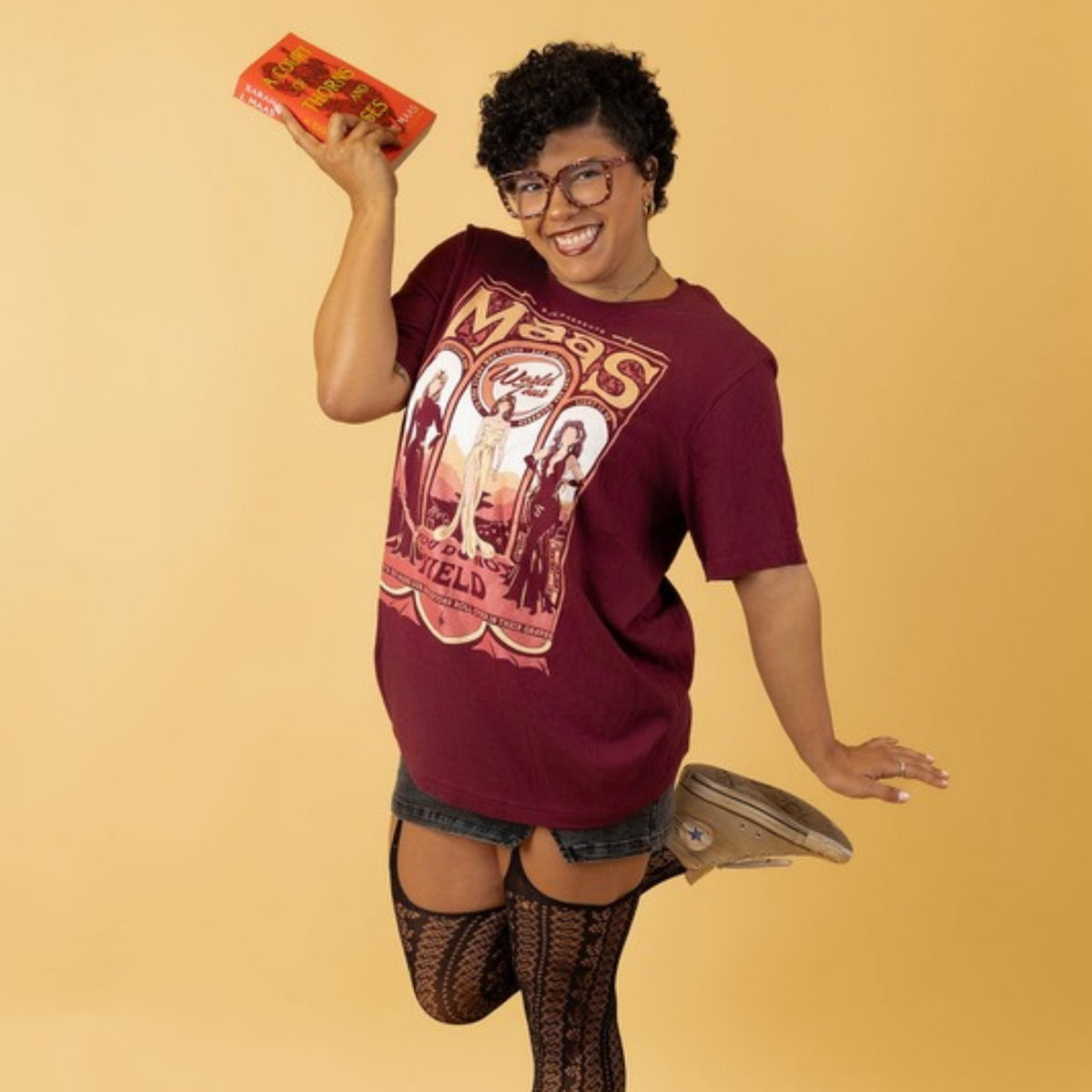 Model jumping with a book in the maroon Maas World Tour t-shirt, merch inspired by the worlds of Sarah J. Maas