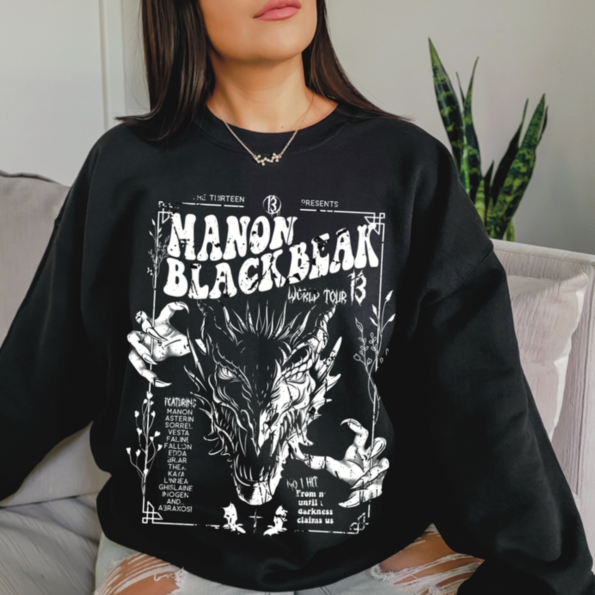 Model on a sofa in the black Manon Blackbeak World Tour sweatshirt, inspired by Throne of Glass by Sarah J. Maas