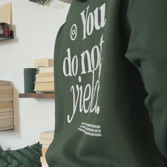 Try-on video: forest green You Do Not Yield hoodie, the cream serif back print reading 'You do not yield.' beneath a circular mark, with the smaller quote block below, and the matching chest print [focal 50 30]