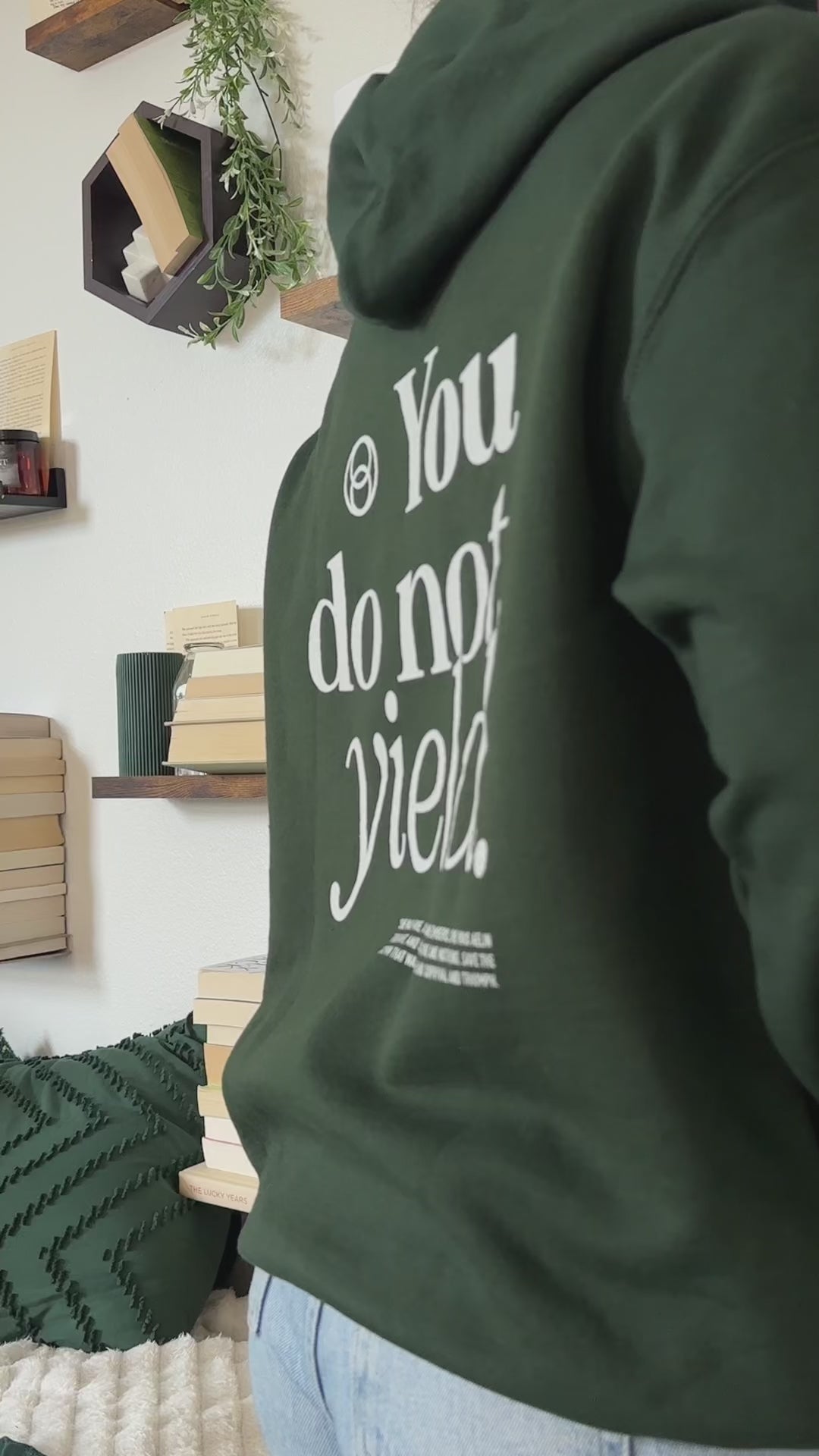 Try-on video: forest green You Do Not Yield hoodie, the cream serif back print reading 'You do not yield.' beneath a circular mark, with the smaller quote block below, and the matching chest print [focal 50 30]