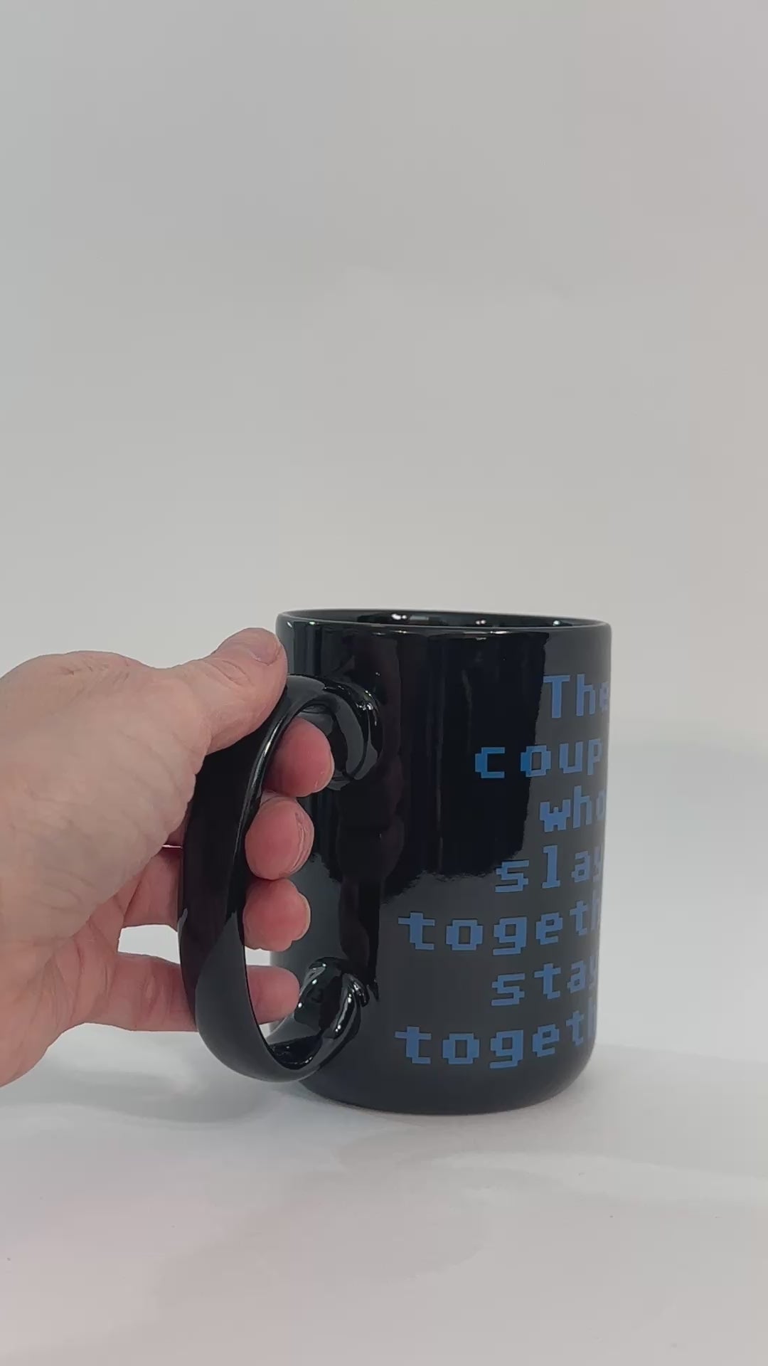 Product video: the black Slay Together Stay Together mug turned by hand — the blue stacked lettering reading 'the couple who slays together stays together' [focal 50 70]