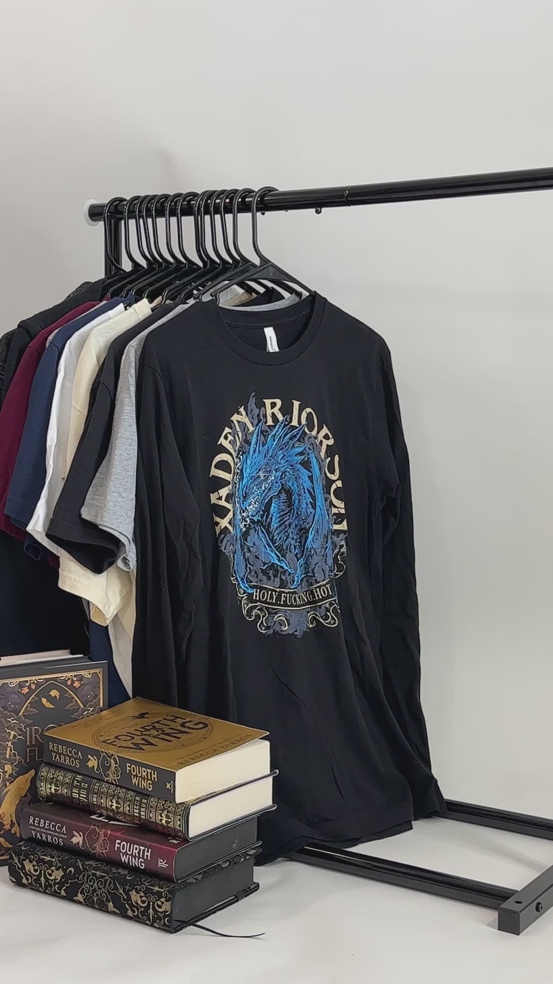 Product video: the black Xaden Riorson t-shirt — the blue dragon in an arched frame with XADEN RIORSON curved around it and 'holy fucking hot' beneath [focal 50 40]
