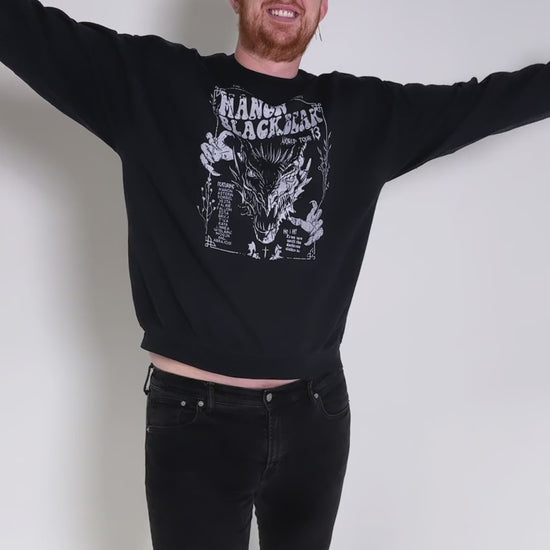 Fit video: four different models wearing the black Manon Blackbeak sweatshirt against a studio backdrop — the white tour-poster print with 'The Thirteen presents', MANON BLACKBEAK, World Tour 13 and the wyvern [focal 50 30]