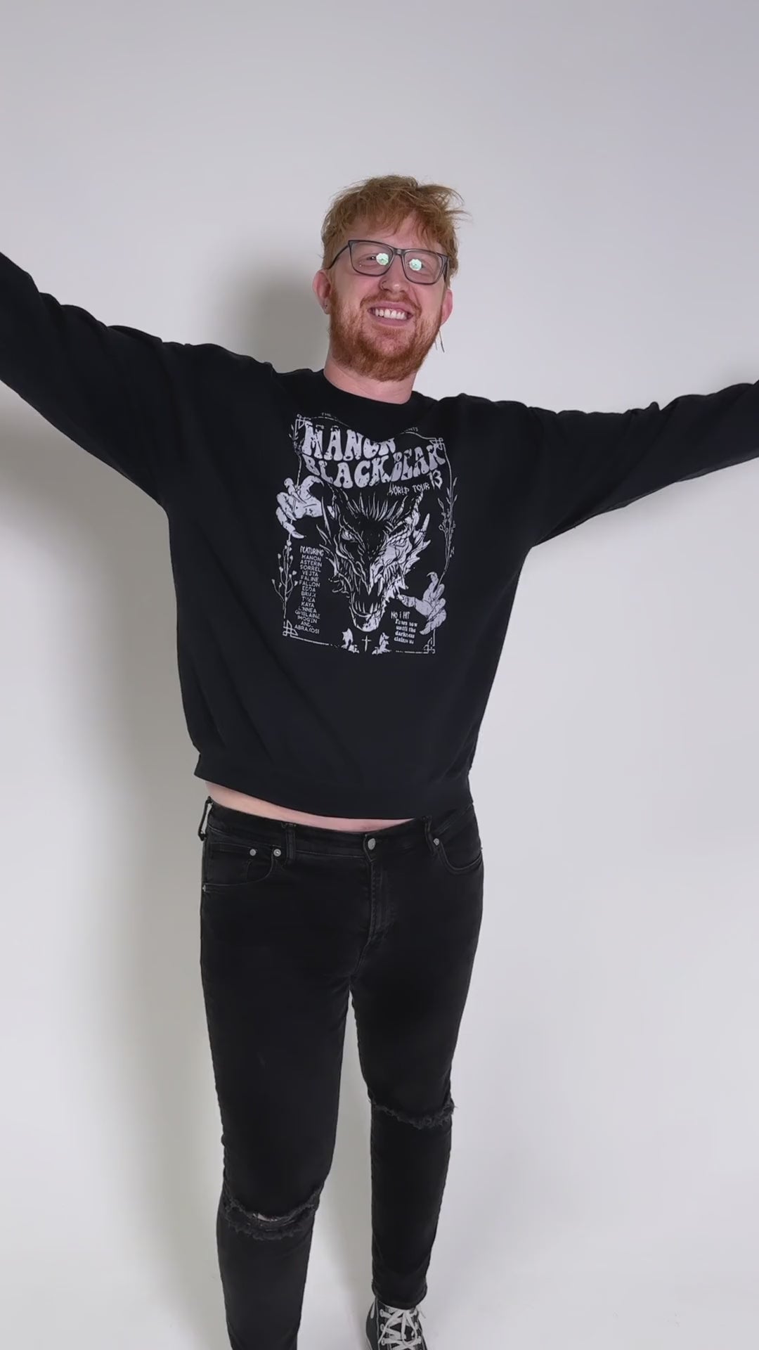 Fit video: four different models wearing the black Manon Blackbeak sweatshirt against a studio backdrop — the white tour-poster print with 'The Thirteen presents', MANON BLACKBEAK, World Tour 13 and the wyvern [focal 50 30]