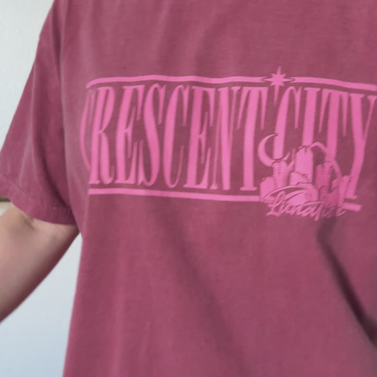 Try-on video: the maroon Crescent City Location t-shirt — the pink outline CRESCENT CITY lettering with the small Lunathion mark beneath [focal 50 40]