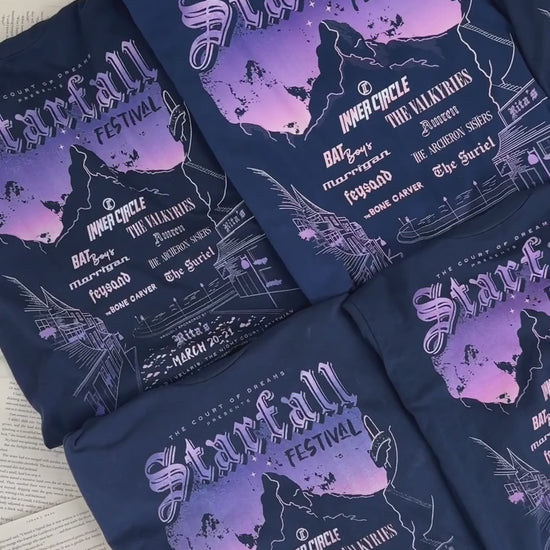 Product video: the navy Starfall Festival t-shirts folded — the lilac and peach mountain poster with the Inner Circle line-up beneath the Starfall Festival lettering [focal 50 40]