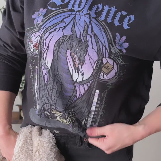 Try-on video: the black Violence sweatshirt, then in close on the print — the stained-glass arch in purple and lilac around the dark winged dragon, with Violence in gothic script above [focal 50 30]