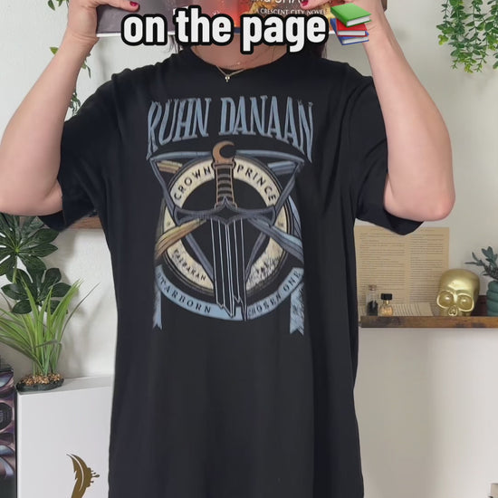 Try-on video: the black Ruhn Danaan t-shirt — the RUHN DANAAN lettering above the crossed sword and staff with the CROWN PRINCE roundel [focal 50 42]