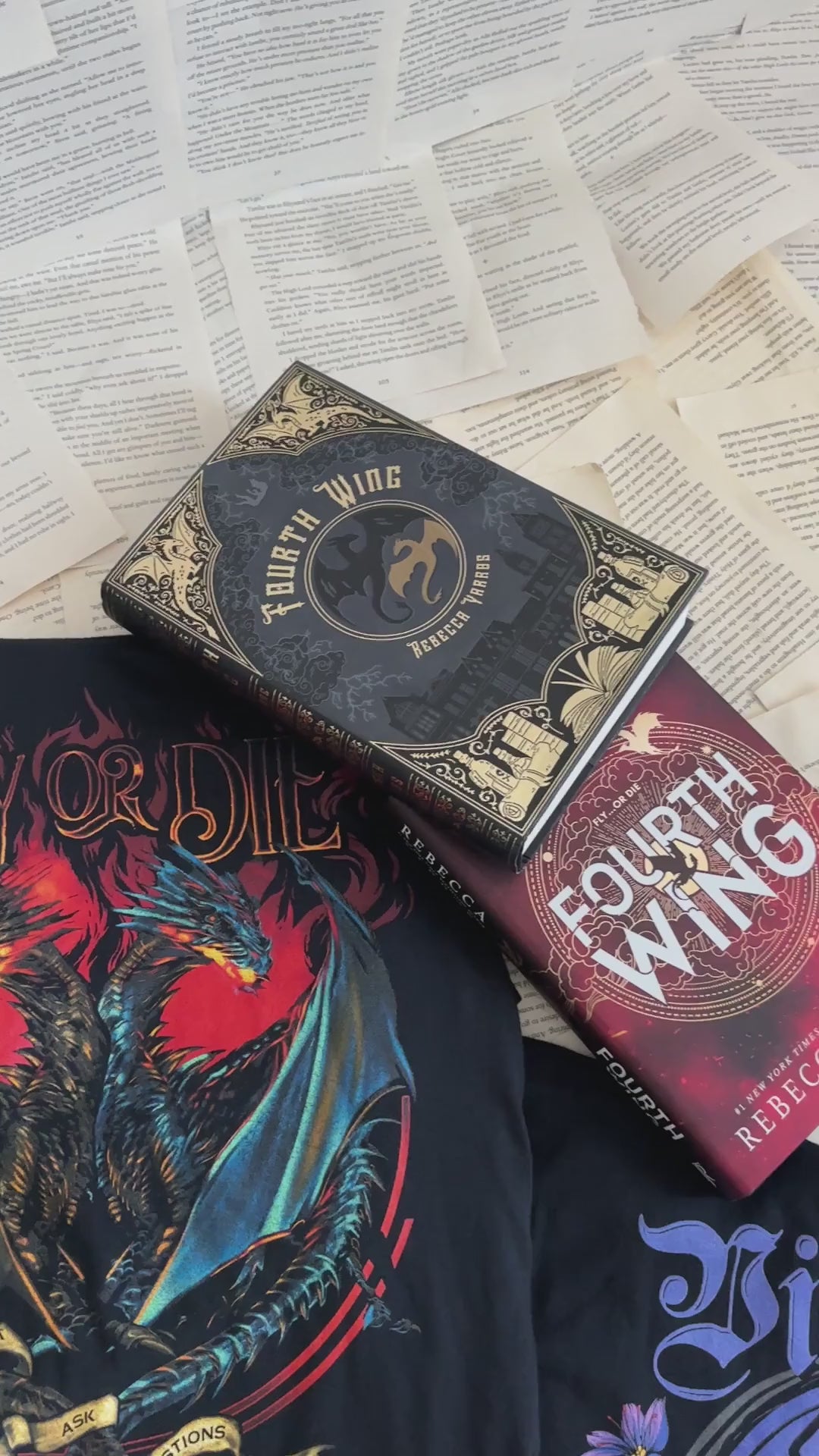 Flat lay video: the black Fly or Die t-shirt with the Fourth Wing and Iron Flame hardbacks — the red and blue dragons facing off beneath the FLY OR DIE lettering [focal 50 55]