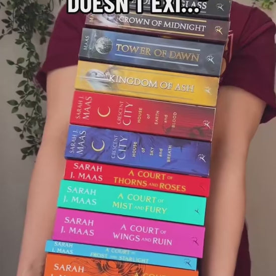 Reveal video: a stack of the whole Sarah J Maas shelf held up over the maroon Maasverse t-shirt, then dropped — the art-nouveau tour poster with MAAS, the World Tour roundel, the three figures in their arches and 'you do not yield' beneath [focal 50 20]