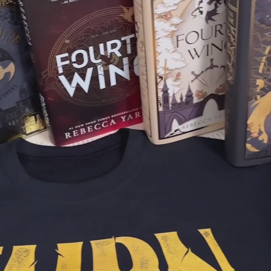 Flat lay video: the black Tairn sweatshirt with the Fourth Wing, Iron Flame and Onyx Storm hardbacks above it — the gold gothic TAIRN lettering over the white line-art dragon [focal 50 45]