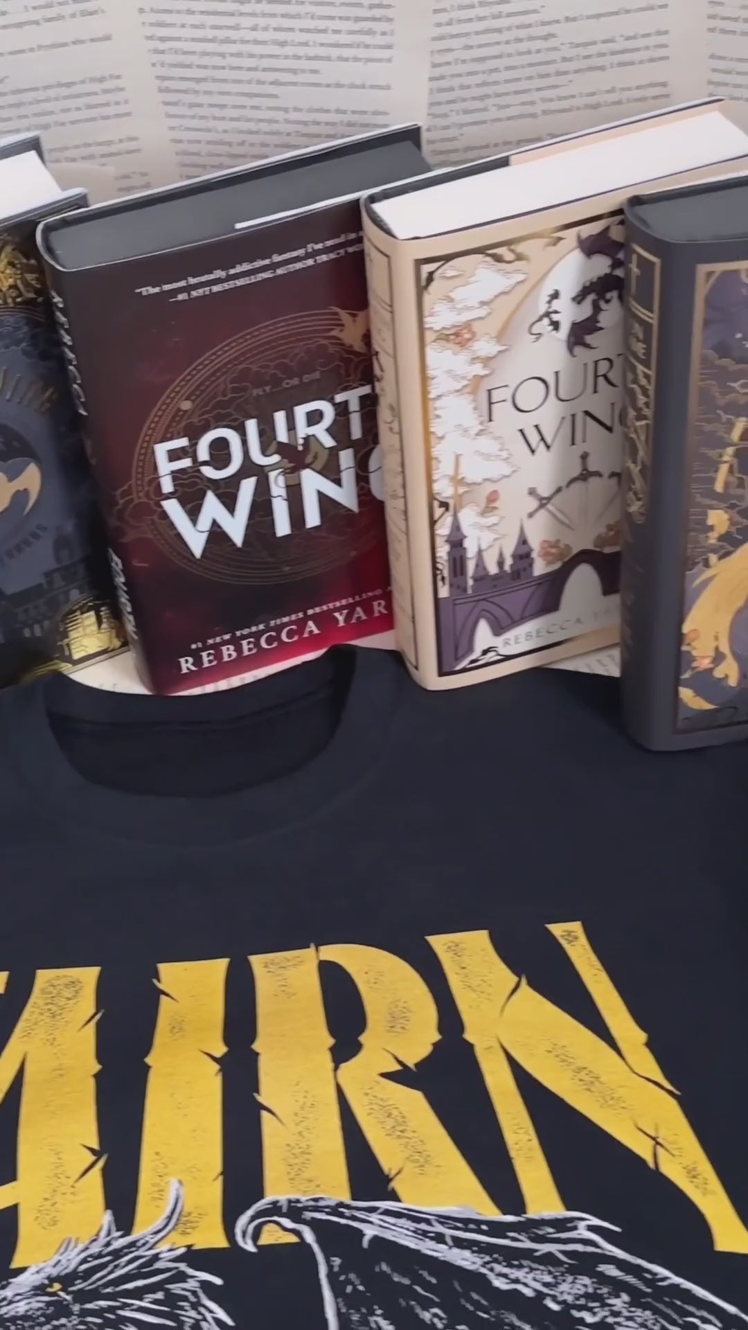 Flat lay video: the black Tairn sweatshirt with the Fourth Wing, Iron Flame and Onyx Storm hardbacks above it — the gold gothic TAIRN lettering over the white line-art dragon [focal 50 45]