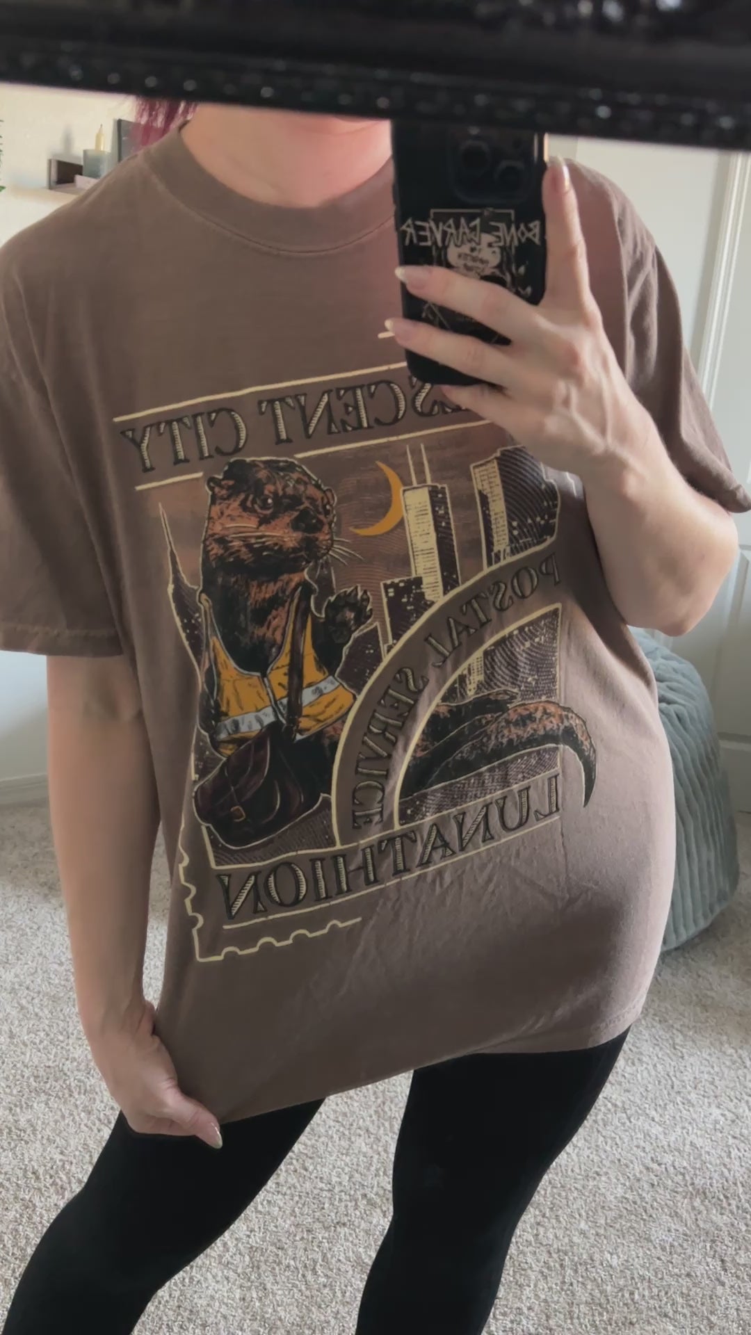 Mirror try-on video: oversized taupe Crescent City Otters t-shirt worn with leggings, the arched gold and dark print with the otters filling the chest [focal 50 35]