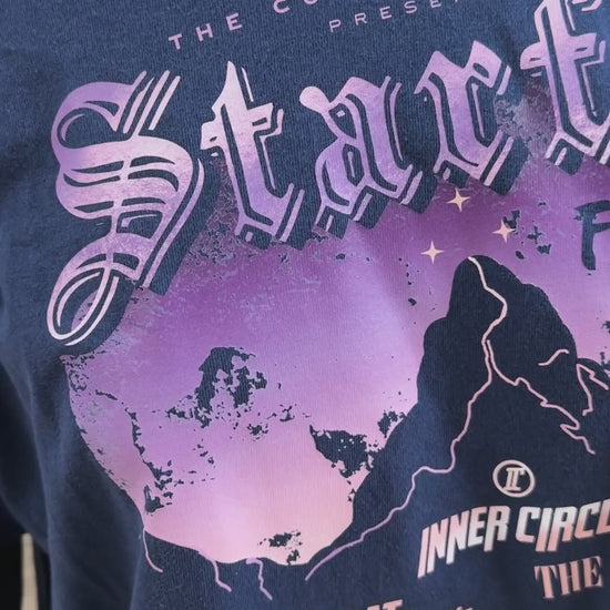Detail video: the print on the navy Starfall Festival sweatshirt — the lilac and peach sky behind the mountain, and the Inner Circle line-up beneath: Bat Boys, The Valkyries, Morrigan, Feysand, The Bone Carver, The Suriel [focal 50 45]