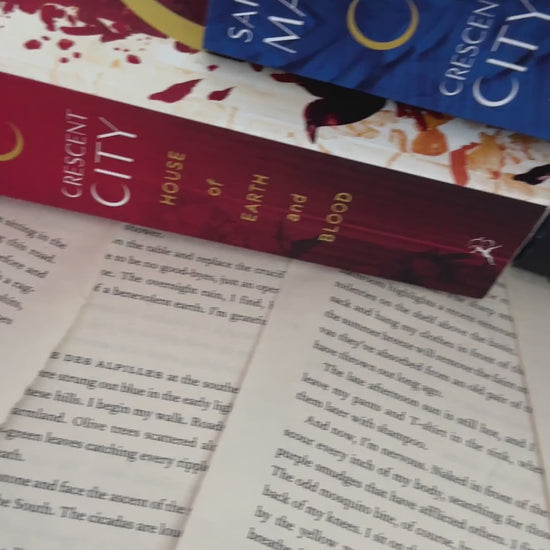 Lifestyle video: the Crescent City hardbacks, then the maroon Greetings From Crescent City sweatshirt — the blush skyline arch with 'Lunathion' and 'Light it up' beneath [focal 50 50]
