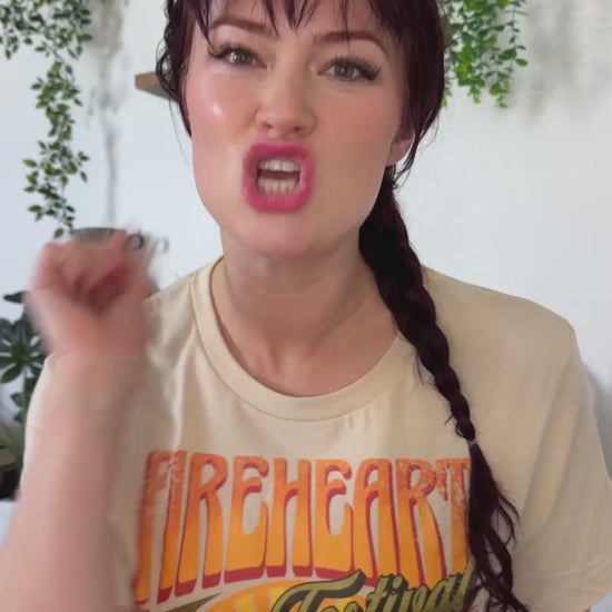 Try-on video: cream Fireheart Festival t-shirt with the retro Beltane poster print, worn with jeans and held beside a Throne of Glass hardback by Sarah J. Maas [focal 50 58]