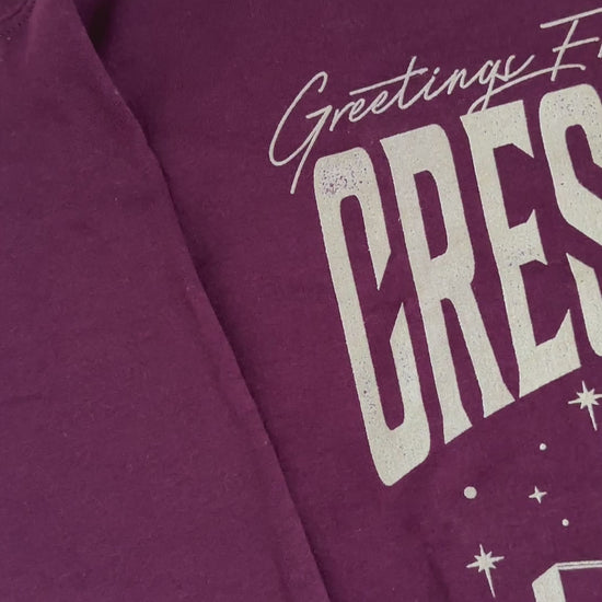 Flat lay video: the maroon Greetings From Crescent City sweatshirt — the blush skyline arch with 'Lunathion' and 'Light it up' beneath the lettering [focal 50 55]