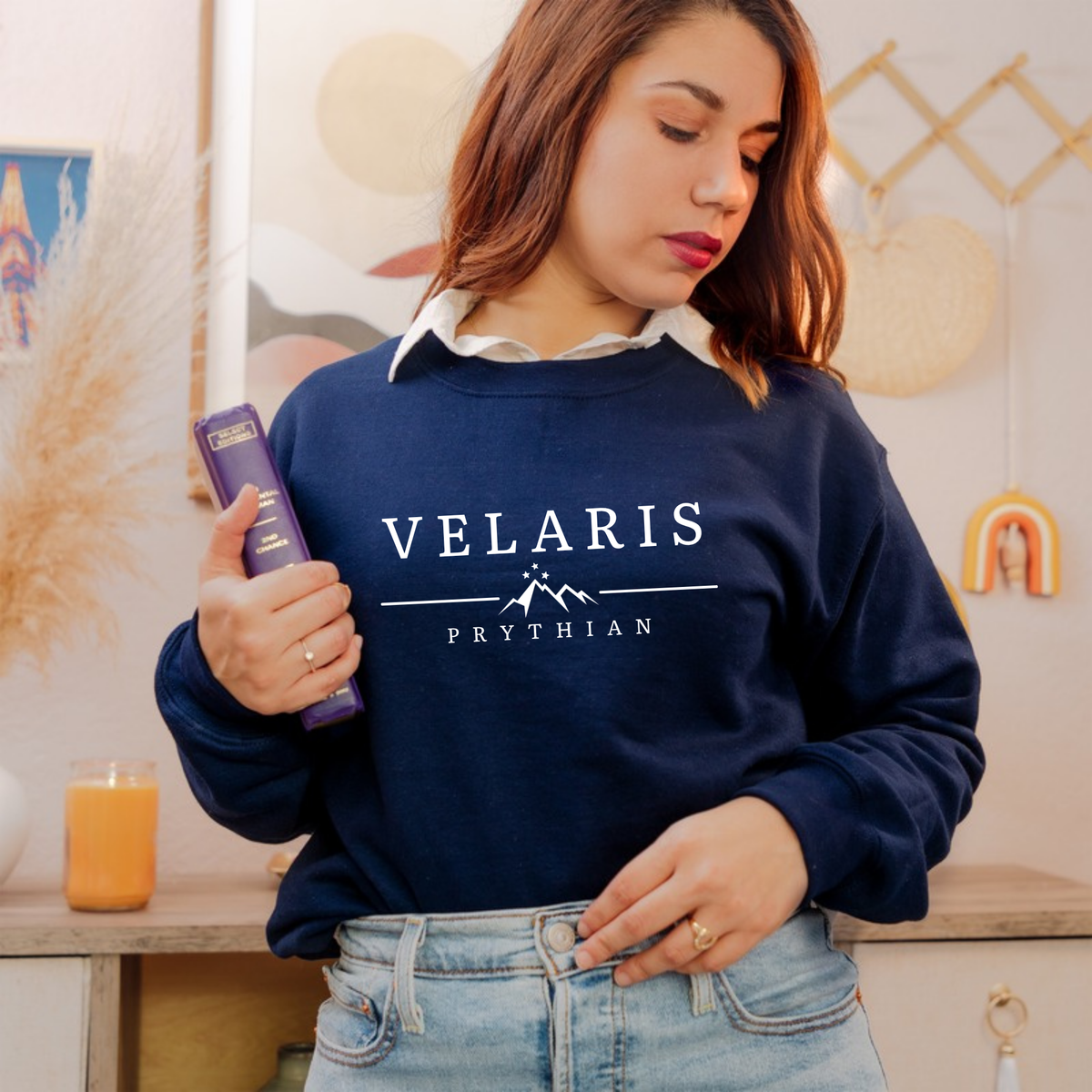 Model holding a book in a navy Velaris Prythian sweatshirt, ACOTAR merch inspired by Sarah J. Maas