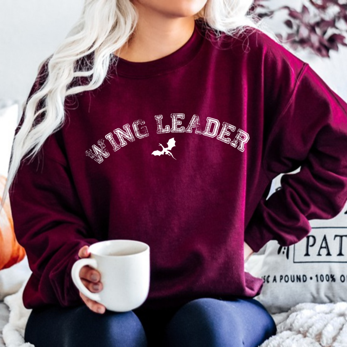 Model holding a mug in a maroon Wing Leader sweatshirt with distressed arched lettering and a wyvern, inspired by Throne of Glass by Sarah J. Maas
